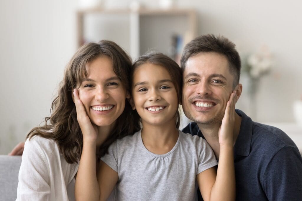 happy loving family flashing smiles, little girl in between parents