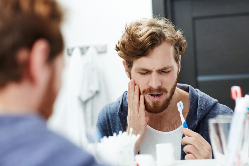 man brushing his teeth in the mirror, sensitive teeth